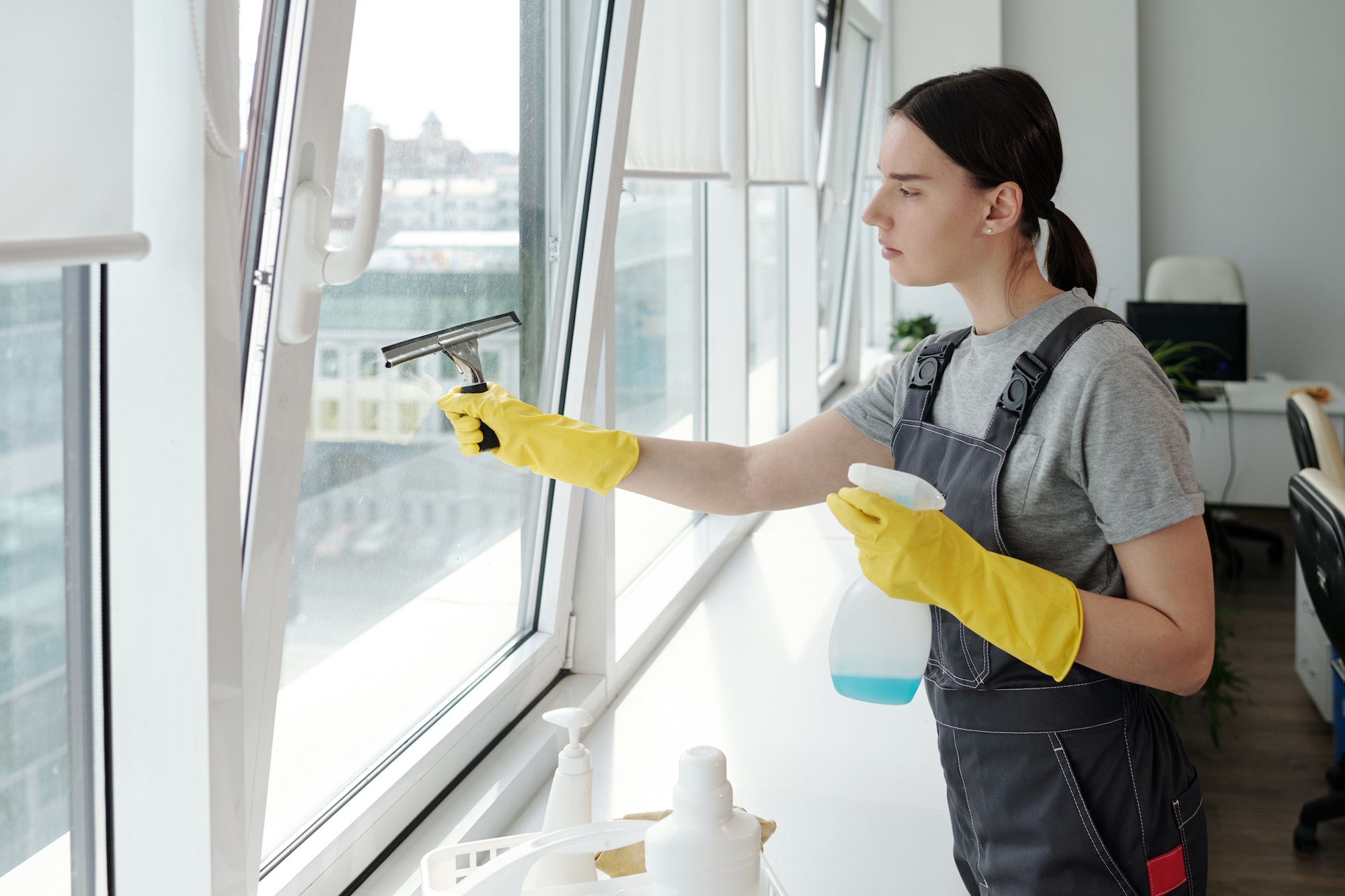 Young female staff of cleaning company washing large window with spatula